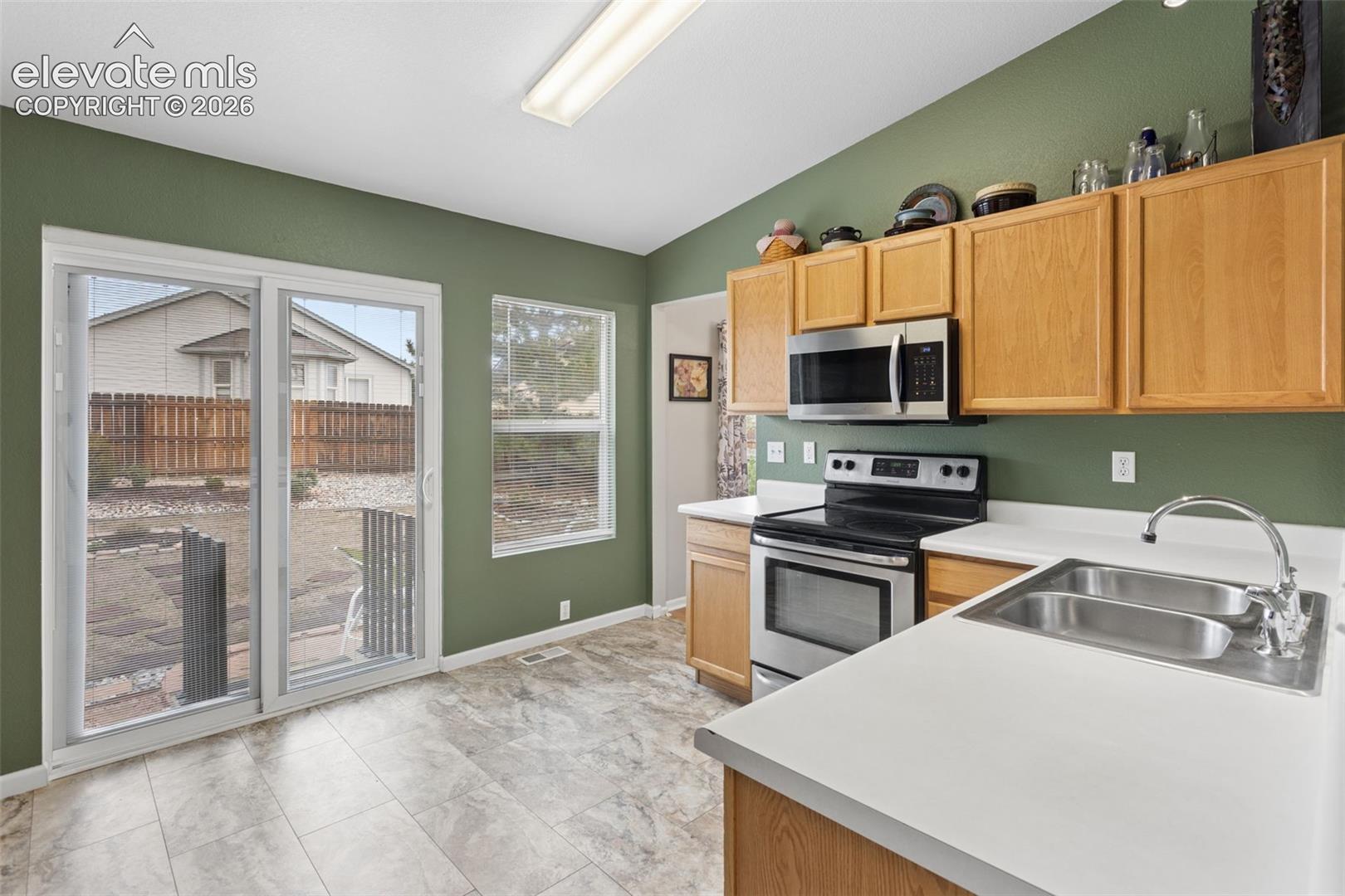 Kitchen featuring wood-finish cabinetry, stainless steel appliances, and a dual basin sink with walk-out to patio