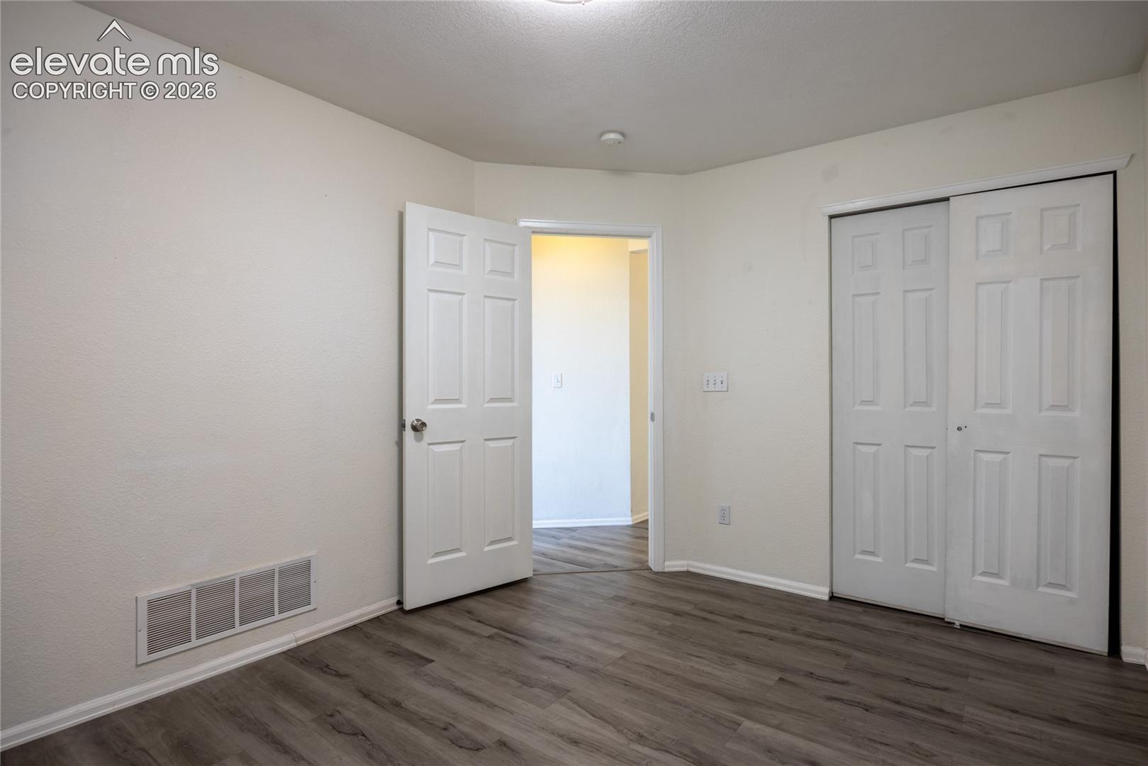 Wood-finish flooring with white baseboards, a white paneled door, and white sliding closet doors