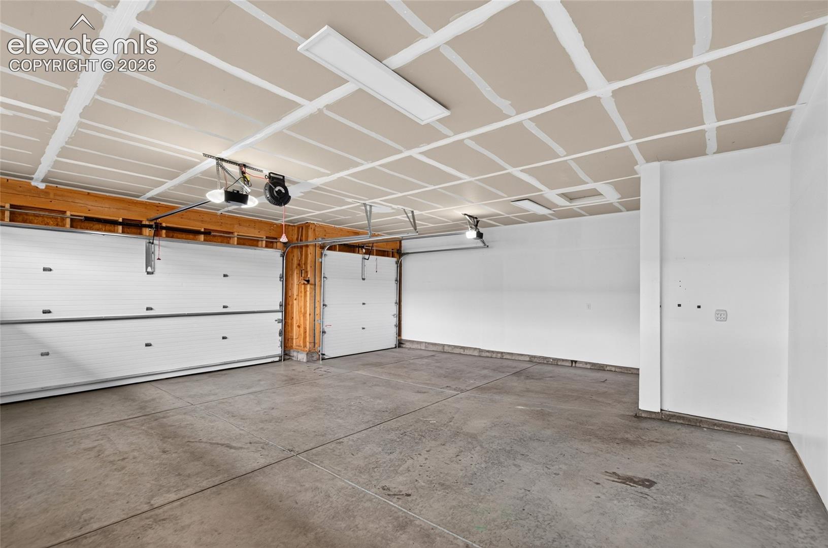 Spacious 4 car tandem garage featuring a concrete floor, white walls, and exposed wood framing