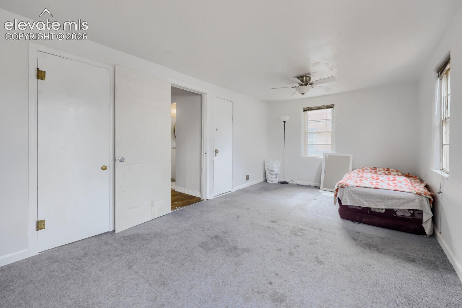 Light grey carpet flooring, white painted walls, and a ceiling fan with light fixture