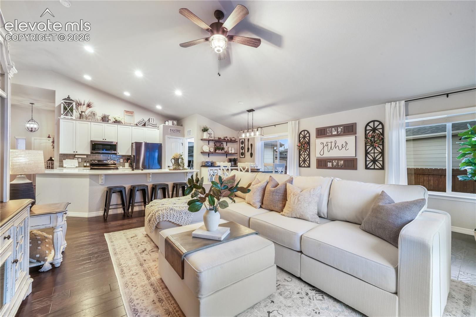 Vaulted ceilings with a ceiling fan, recessed lighting, wood-finish flooring, and a kitchen island with seating
