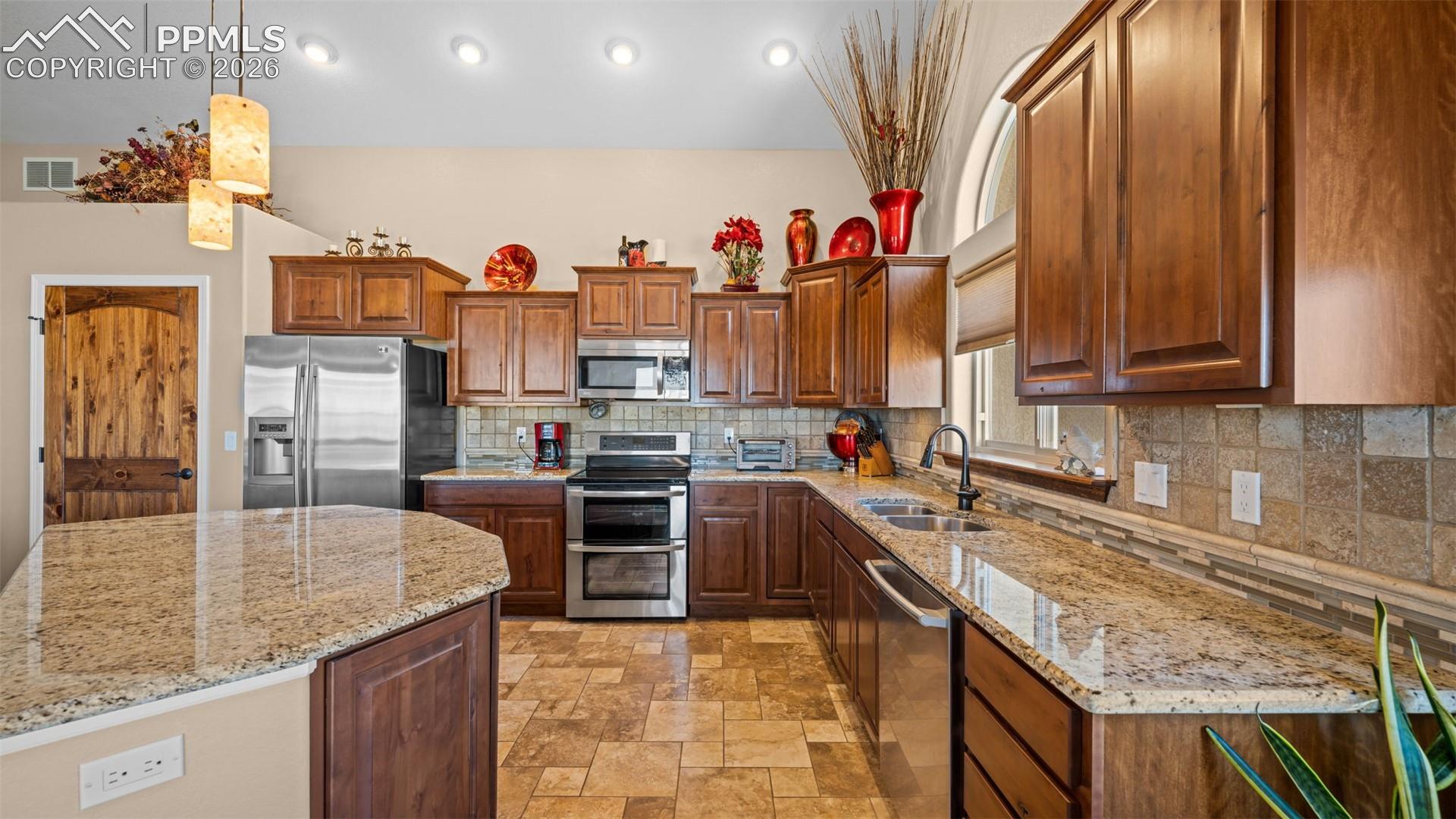 Kitchen featuring stainless steel appliances, a kitchen island, decorative backsplash, granite countertops, and light stone finish floors