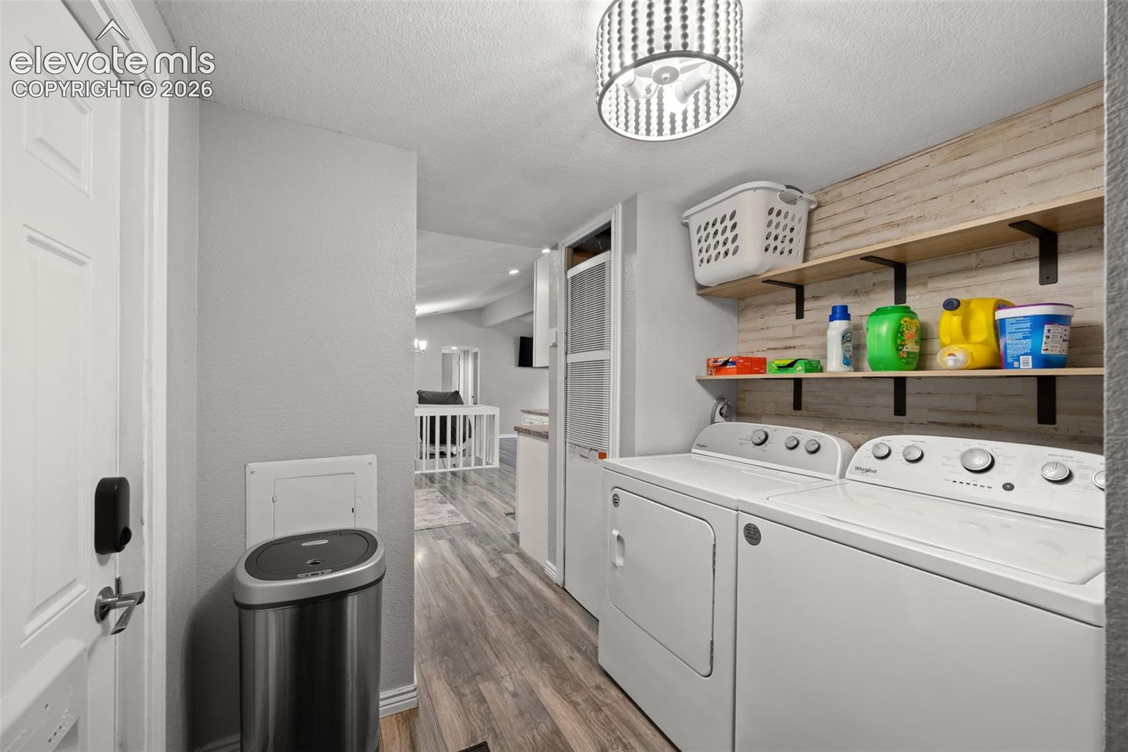 Laundry room featuring wood-finish flooring, floating wood shelving, a textured wall accent, and a decorative drum light fixture