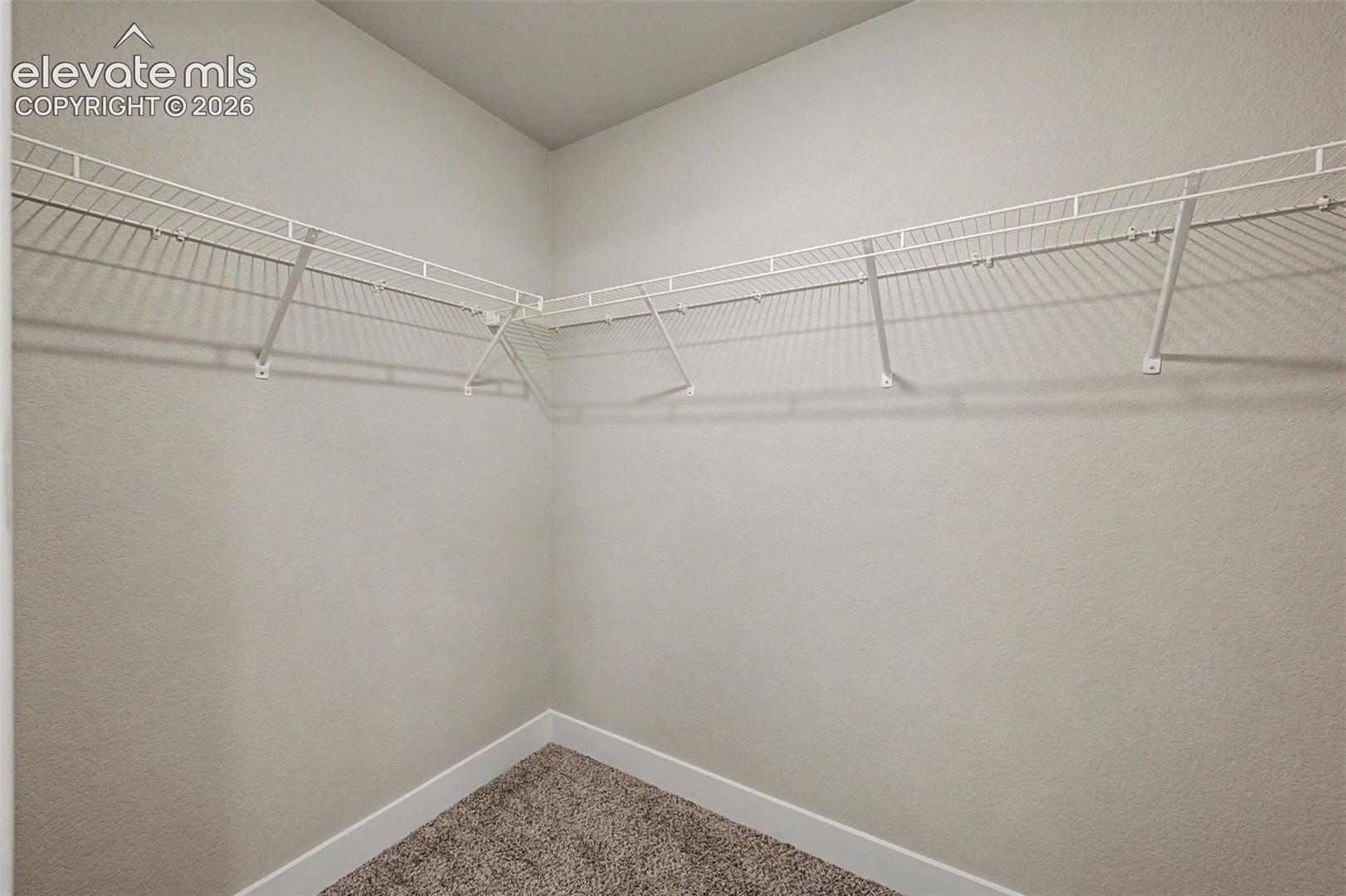 Corner closet with wire shelving system, textured wall finish, white baseboards, and carpet flooring