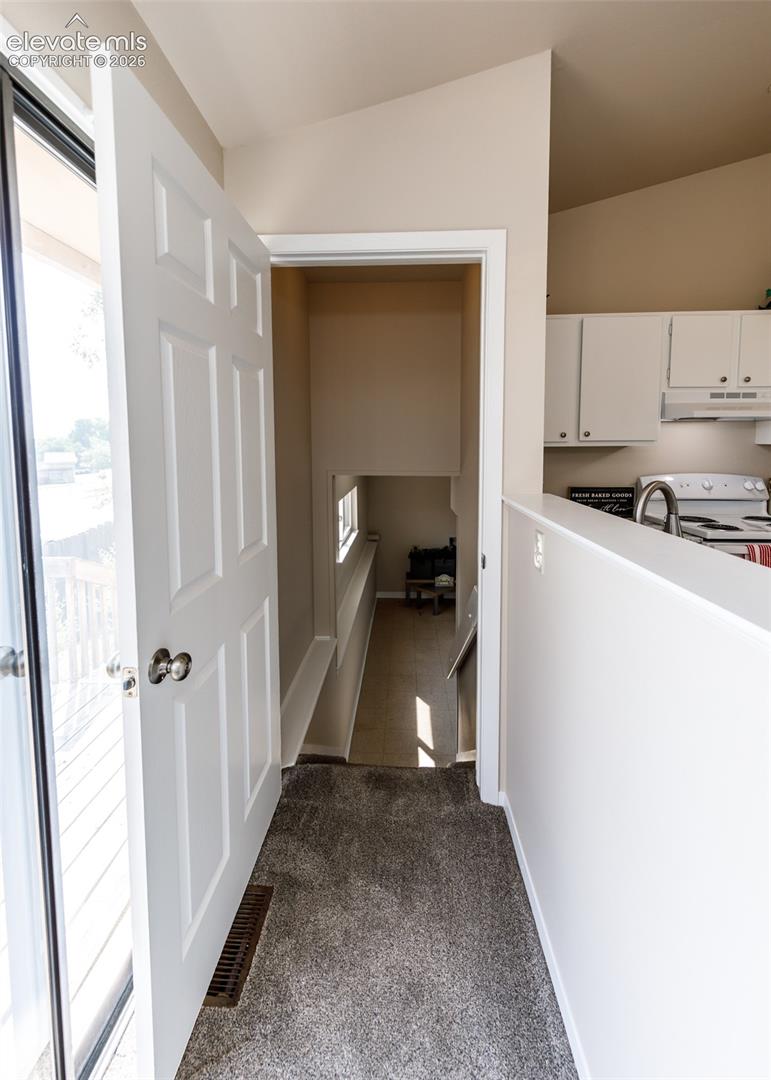 Neutral tone wall paint, vaulted ceiling, white interior doors, gray carpet flooring, white kitchen cabinetry