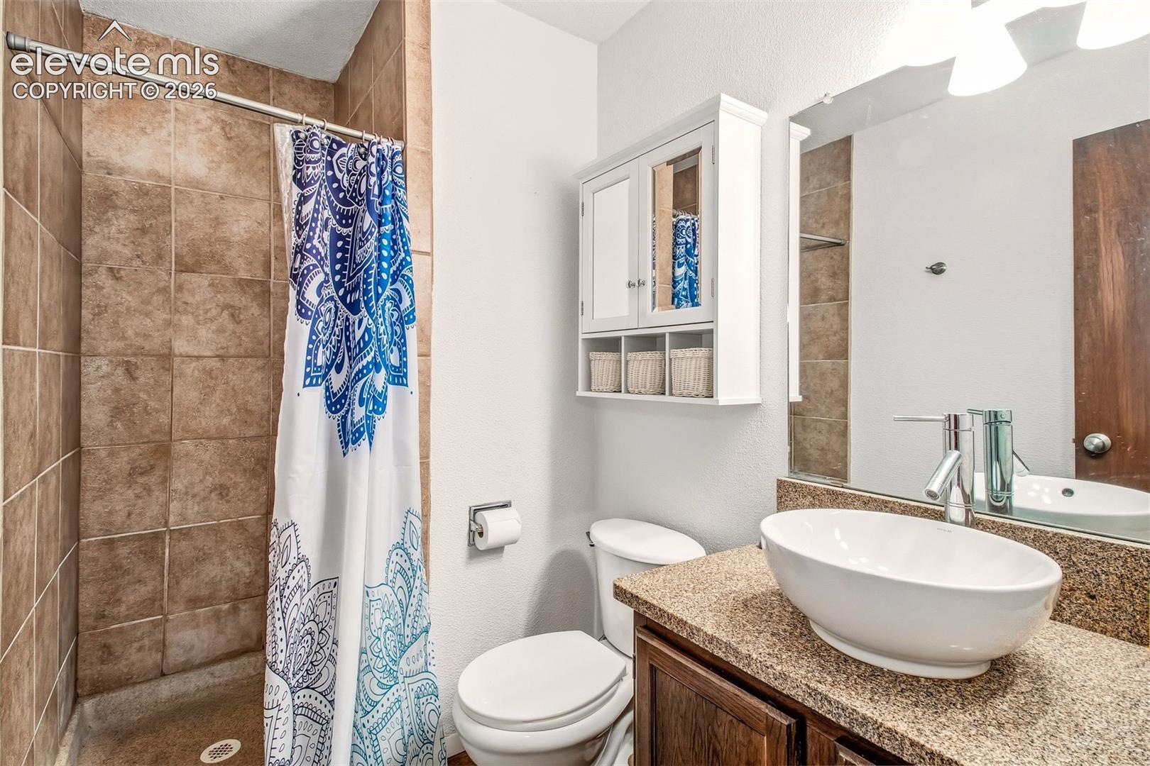 Bathroom featuring a shower stall with full-height tile surround, vessel sink, stone-finish countertop, wood-finish cabinetry, and white wall-mounted medicine cabinet