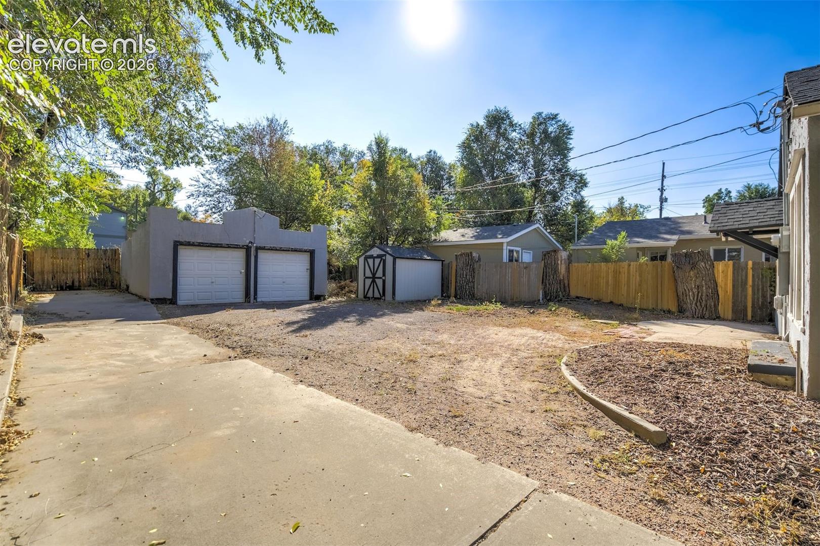 Concrete driveway with a detached two-car garage, secondary storage structure, and fenced perimeter