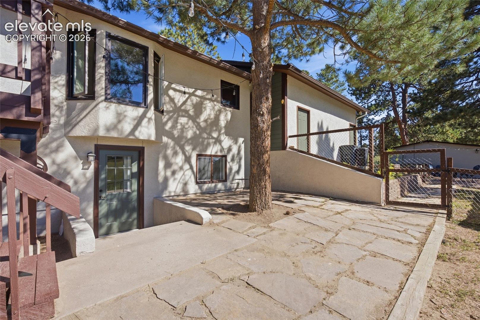 Stucco exterior with a bay window, natural stone patio, concrete walkway, and wood fencing