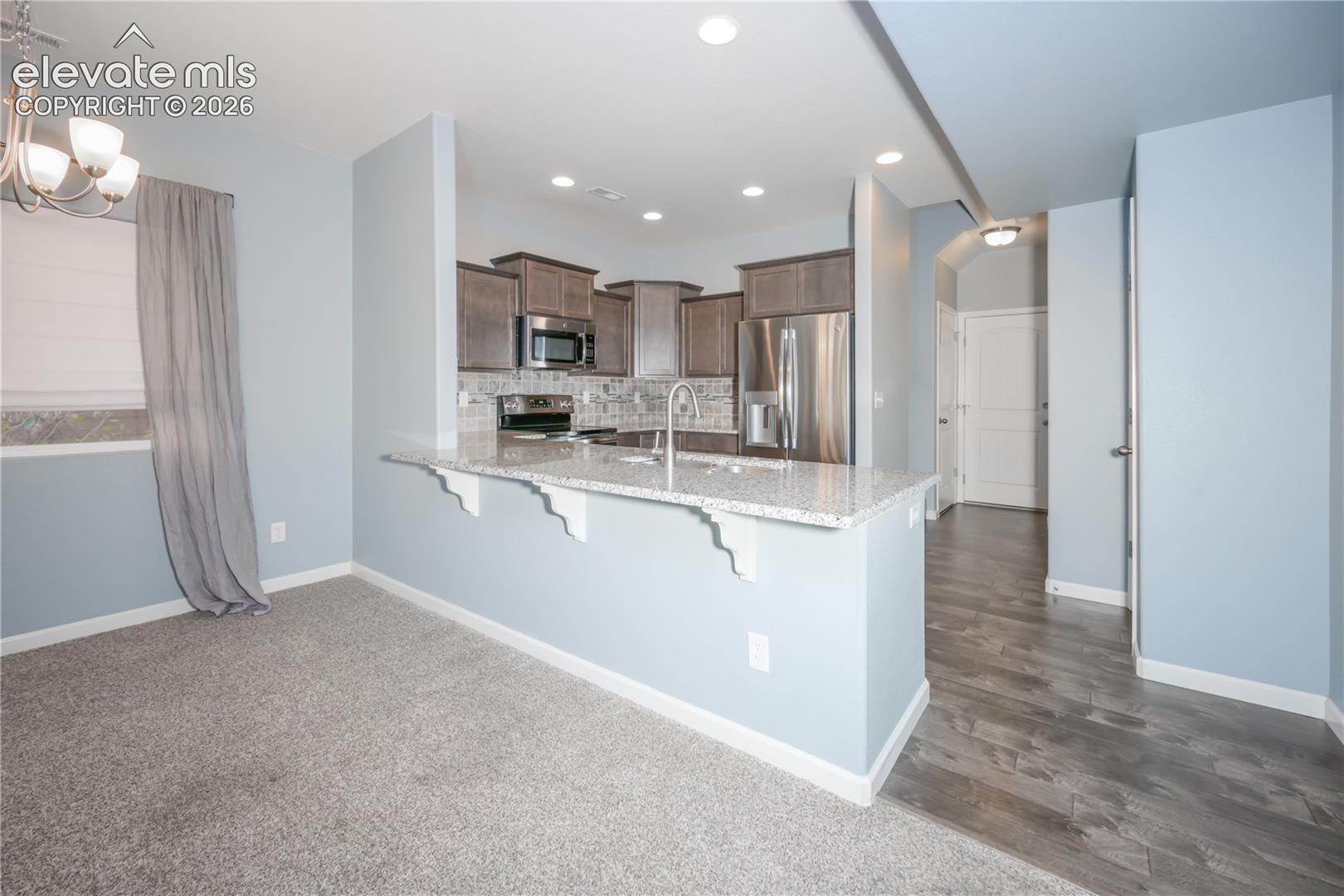 Kitchen featuring cabinetry with crown molding, stone-patterned countertops, stainless steel appliances, a peninsula breakfast bar, and recessed lighting
