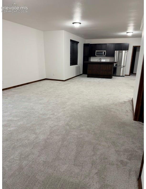 Open-concept living area featuring light-toned carpeting, white walls, and a modern kitchen area