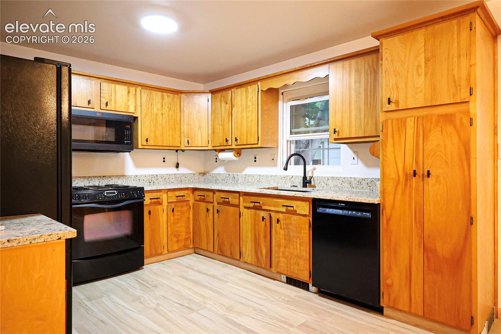 Kitchen featuring wood-finish cabinetry, granite-style countertops, wood-finish flooring, and black appliances