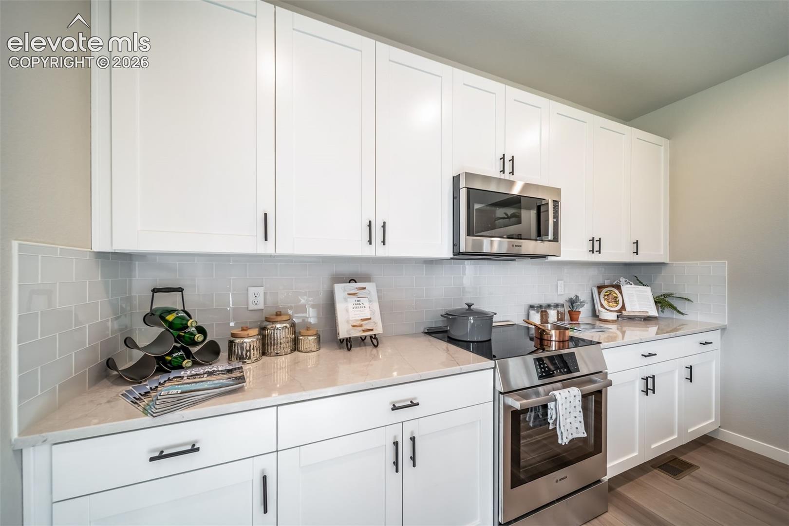 Contemporary kitchen featuring white shaker cabinetry with matte black hardware, light-toned countertops, a subway tile backsplash, and stainless steel appliances including a built-in microwave and electric range
*Photos of a model home*