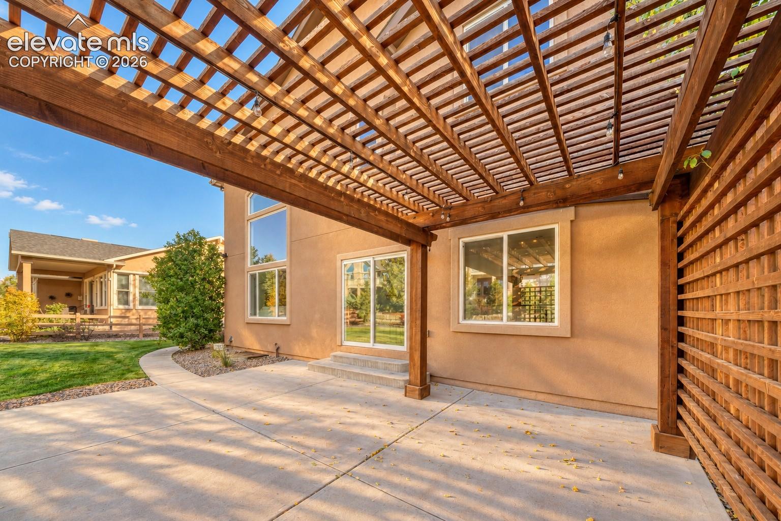 Expansive concrete patio with a wooden pergola structure and an adjacent wooden privacy trellis