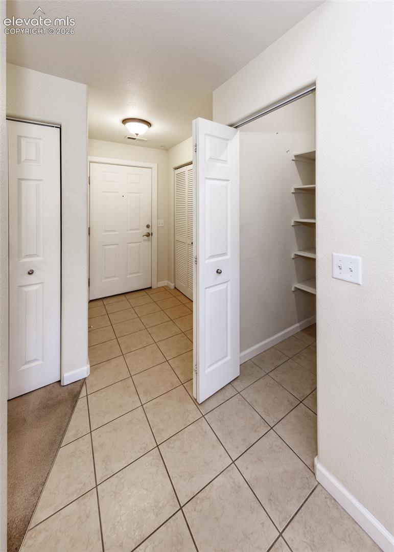 Entryway featuring ceramic tile flooring, a six-panel front door, multiple built-in storage closets, and recessed shelving