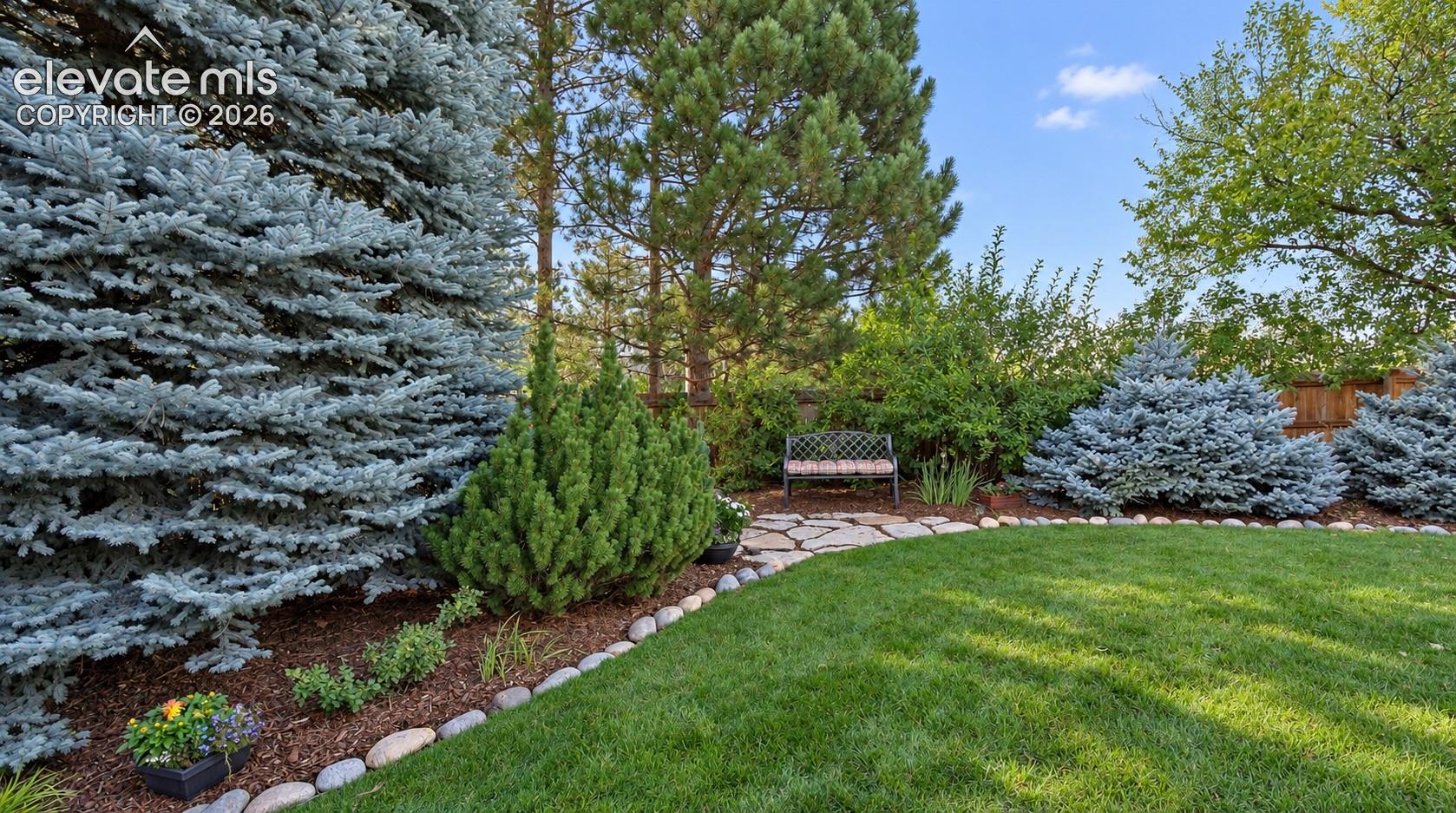 Landscaped garden featuring natural stone hardscaping, manicured lawn, river rock border, and mature coniferous trees