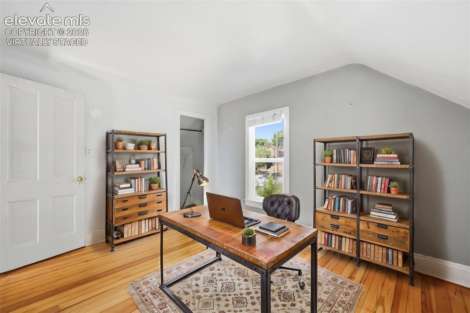 Virtually staged secondary bedroom with pine hardwood flooring, white paneled door, sloped ceiling, and a large single window.