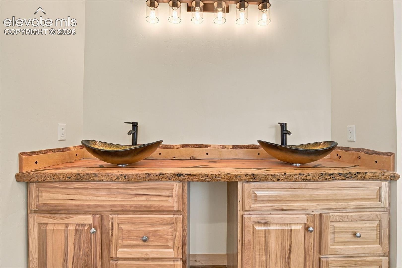 Custom wooden vanity featuring a live-edge countertop, dual vessel sinks, matte black faucets, and a six-light vanity fixture