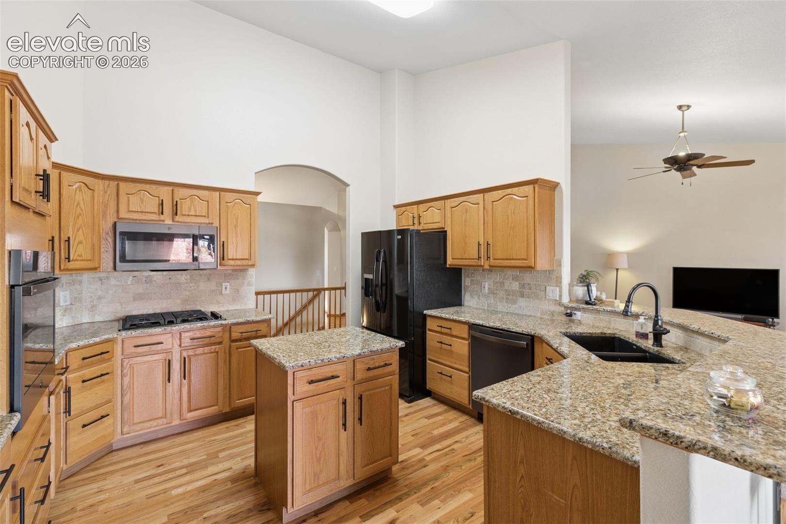 Kitchen featuring vaulted ceilings, wood-finish flooring, stone-style countertops, a center island, and a built-in cooktop