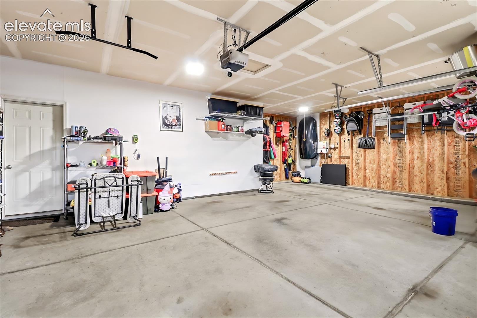 Attached garage featuring concrete flooring, an automated door opener system, wall-mounted storage shelving, and drywall finish