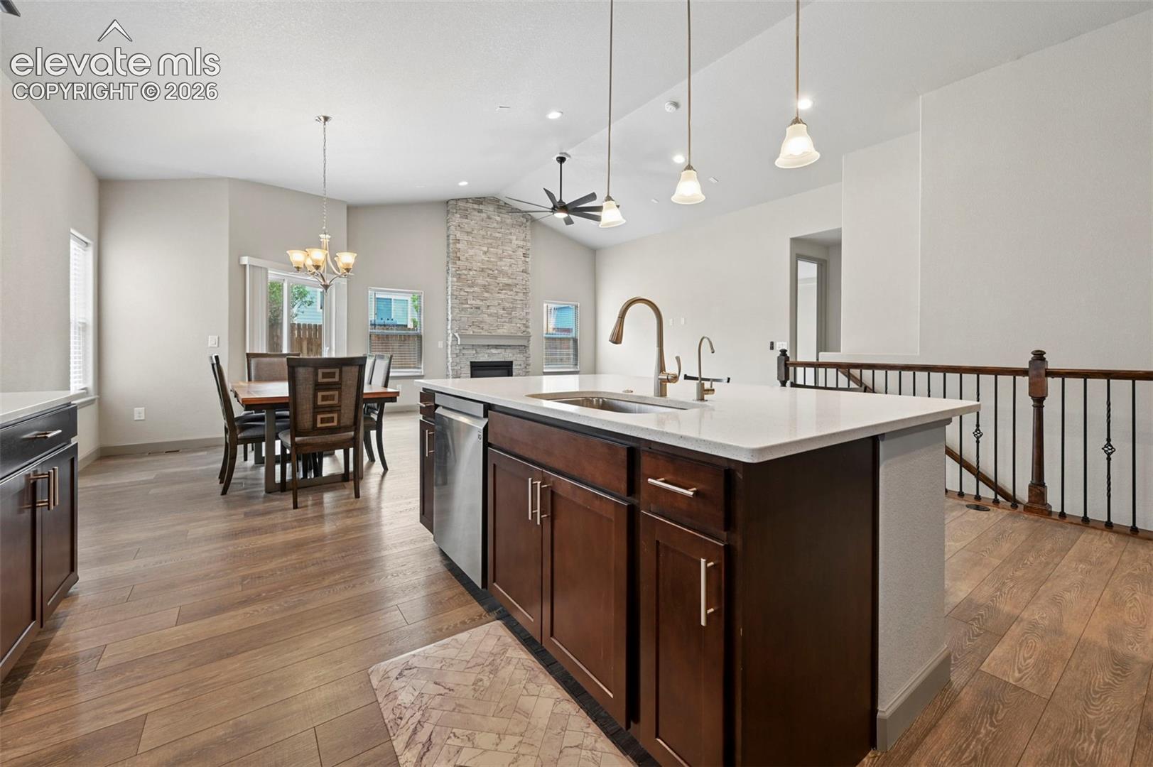 Kitchen featuring a center island with light-toned countertops and stainless steel sink, wood-finish flooring, vaulted ceilings, and a floor-to-ceiling stone-faced fireplace