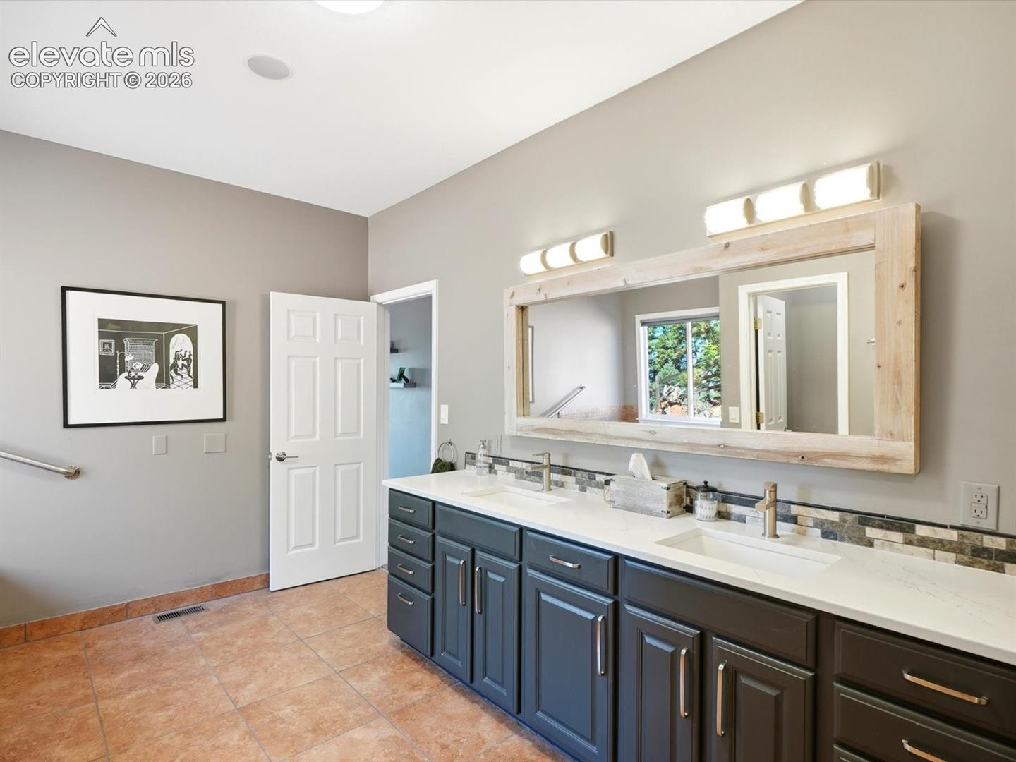 Double vanity with dark cabinetry, stone-finish countertops, undermount sinks, and a custom wood-framed mirror