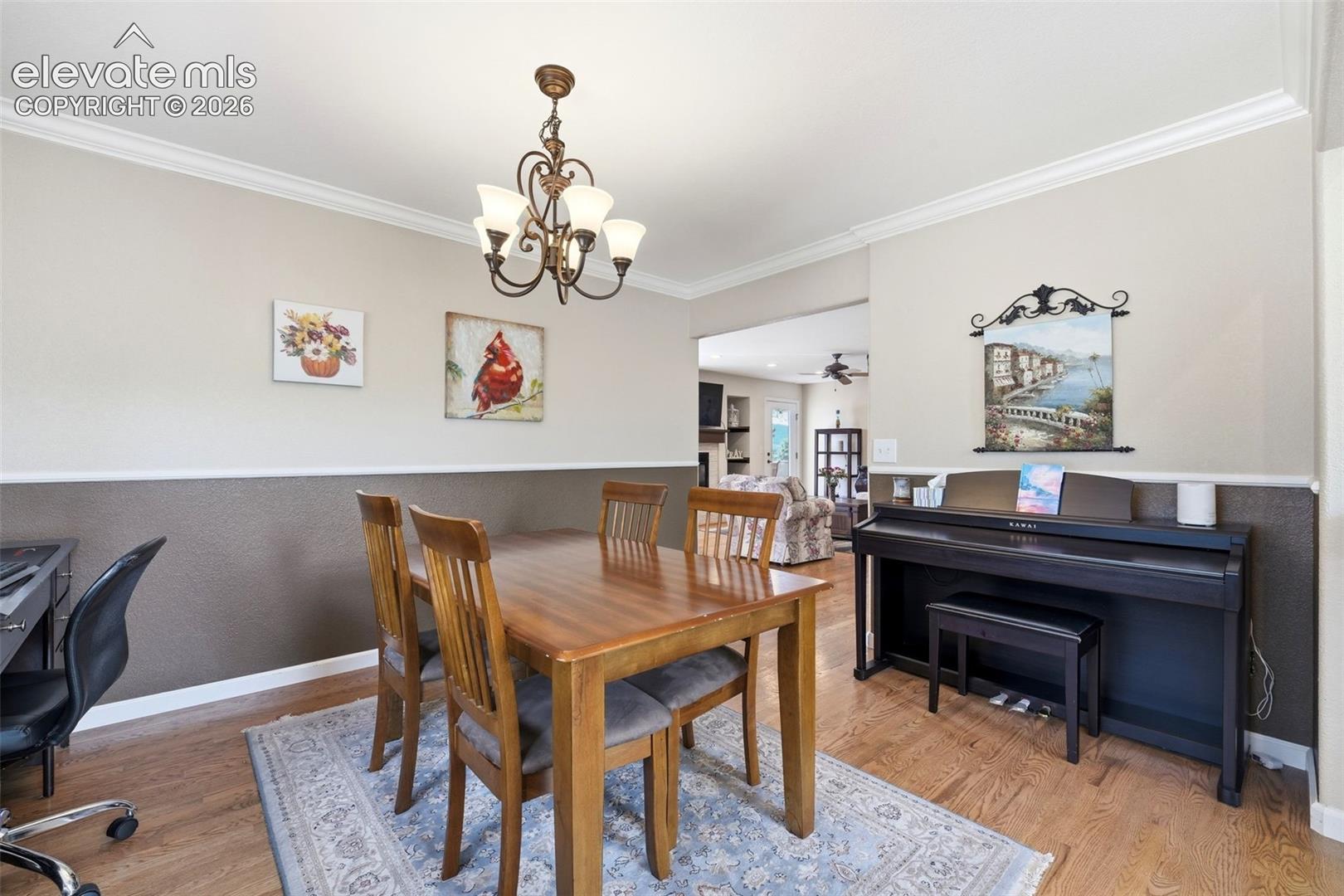 Dining area featuring wood-finish flooring, crown molding, and wainscoting