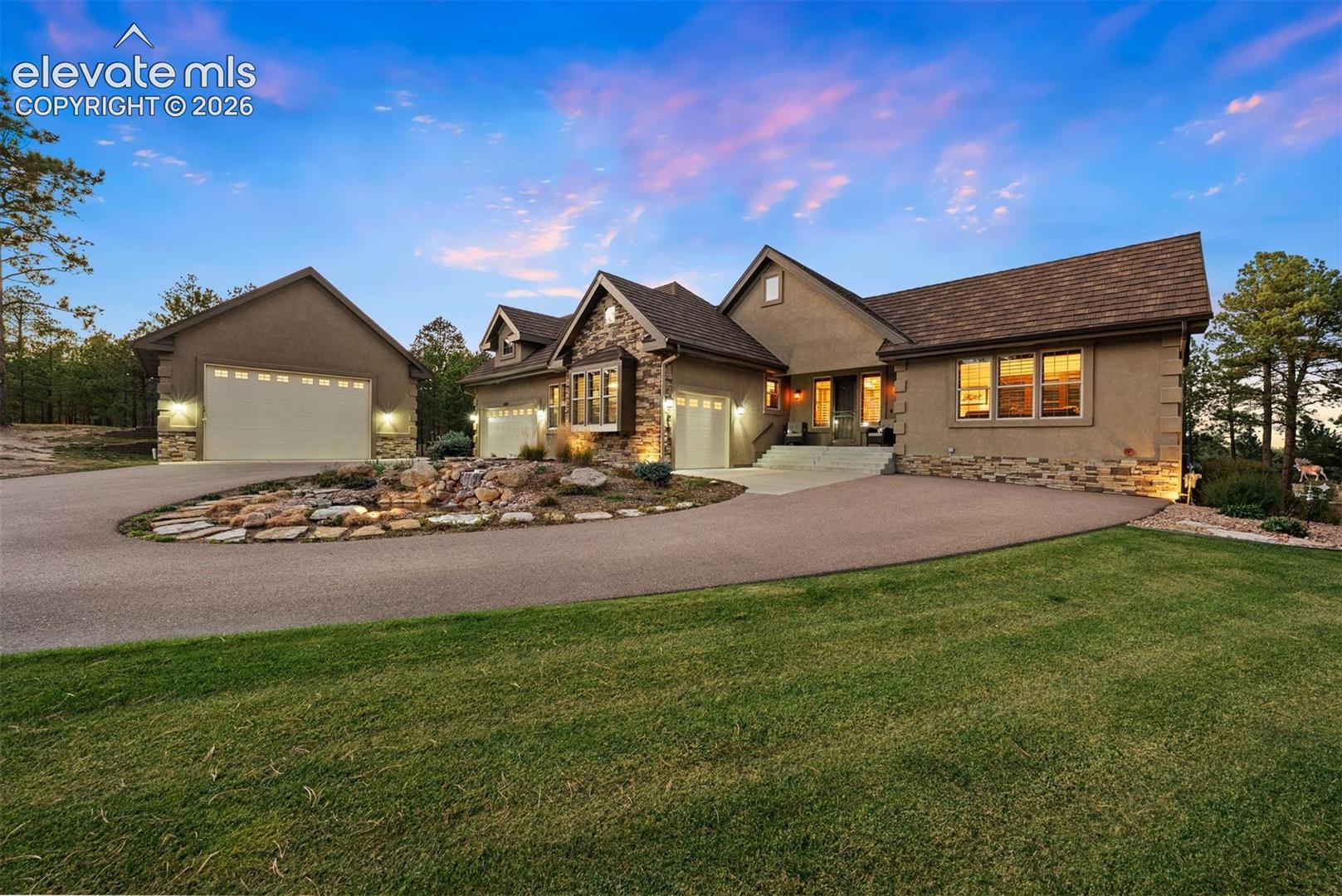 Exterior featuring multi-gabled roofline, stone veneer accents, stucco siding, paved circular driveway, and rock landscaping