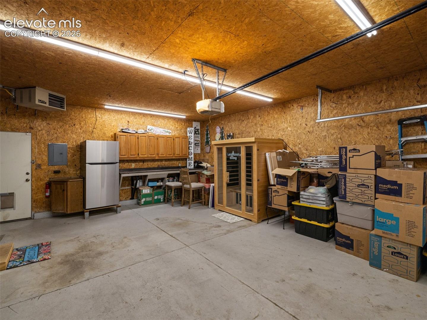 Concrete flooring, wood panel walls, overhead fluorescent lighting, built-in cabinetry, and wall-mounted heating unit