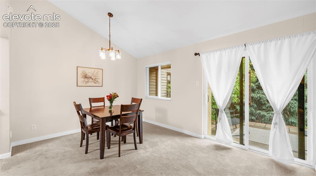Dining area featuring vaulted ceilings, a contemporary chandelier, neutral wall tones, and light-toned carpeting