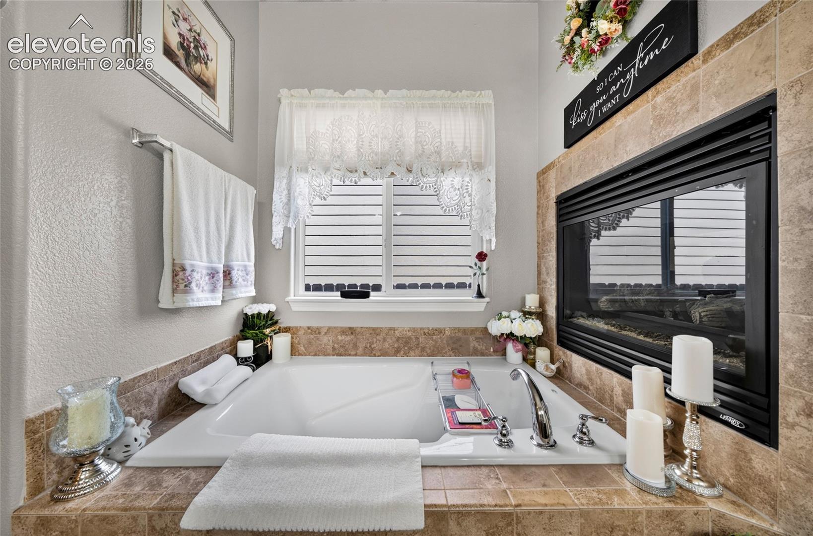 Built-in soaking tub with a tiled surround, integrated fireplace, chrome fixtures, and a single-hung window