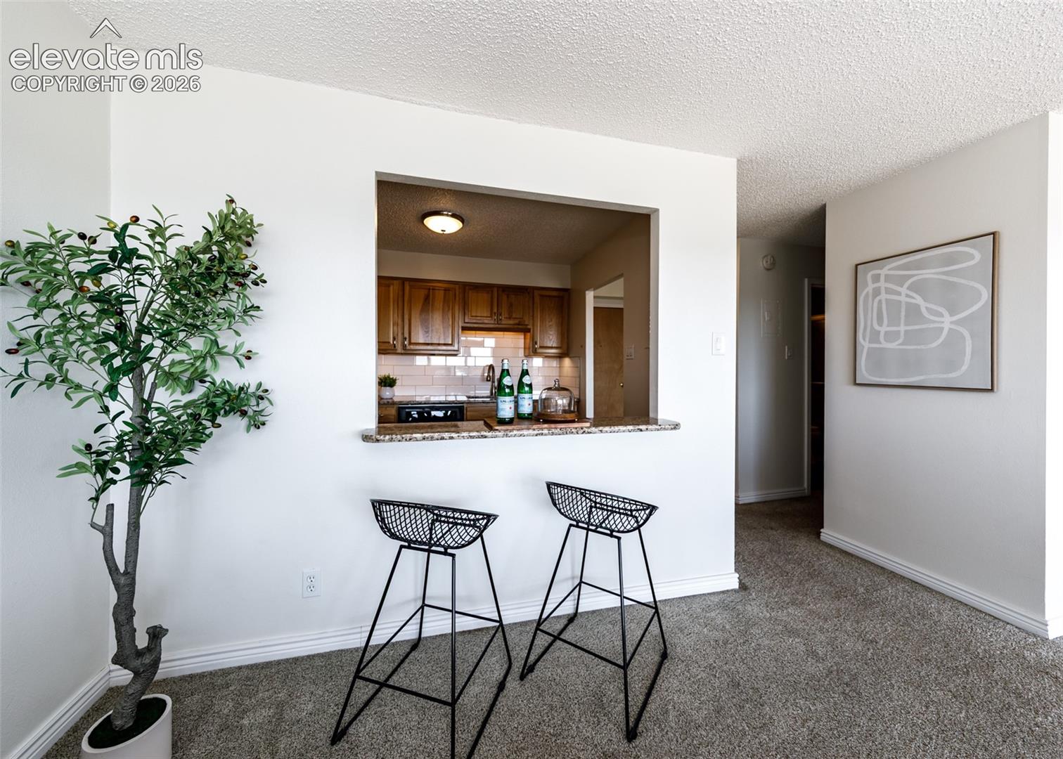 Pass-through kitchen opening with stone-finish countertop, wood-finish cabinetry, and tiled backsplash