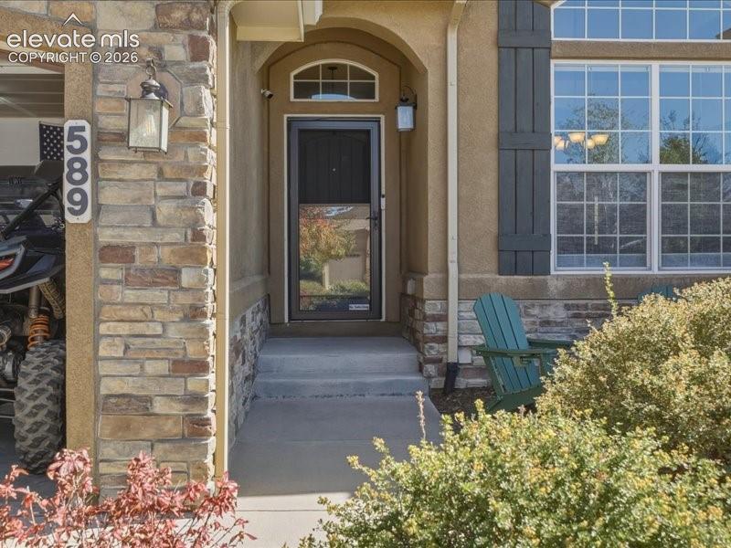 Stone facade detailing, stucco exterior finish, arched entryway, multi-pane windows, and decorative window shutters