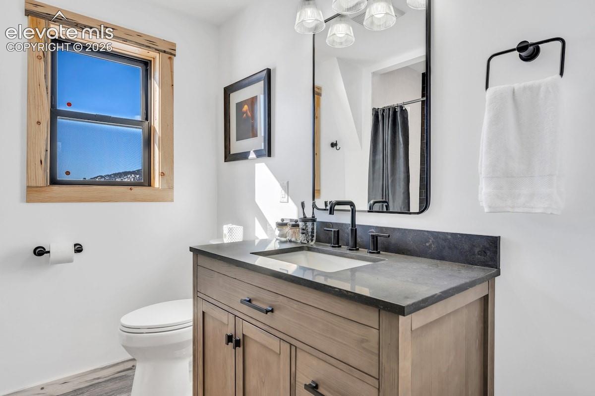 Bathroom vanity featuring a wood-finish cabinet, dark stone countertop, undermount sink, and matte black faucet, complemented by a rustic wood-trimmed window and black-framed mirror