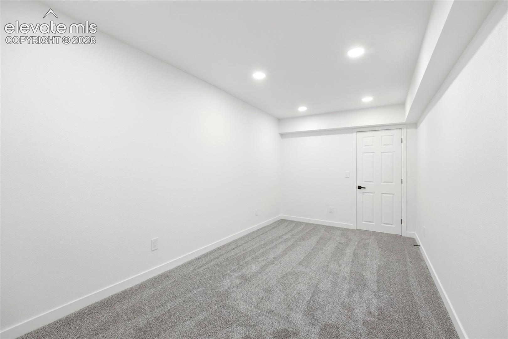 Spacious room featuring neutral carpet flooring, recessed lighting, white trim, and a white four-panel door with matte black hardware
