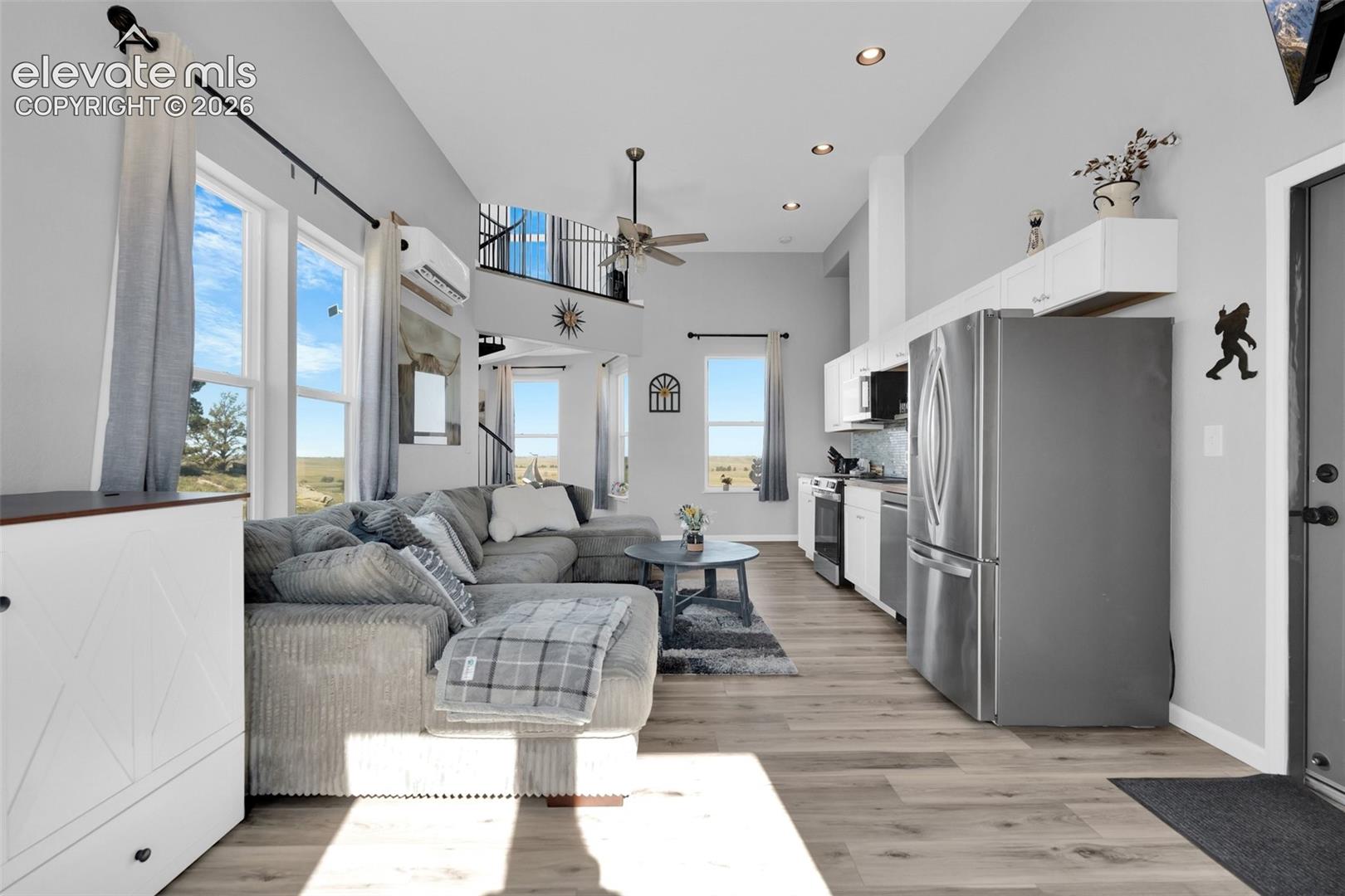 Open-concept interior featuring vaulted ceilings, wood-finish flooring, recessed lighting, white cabinetry, and a metal spiral staircase