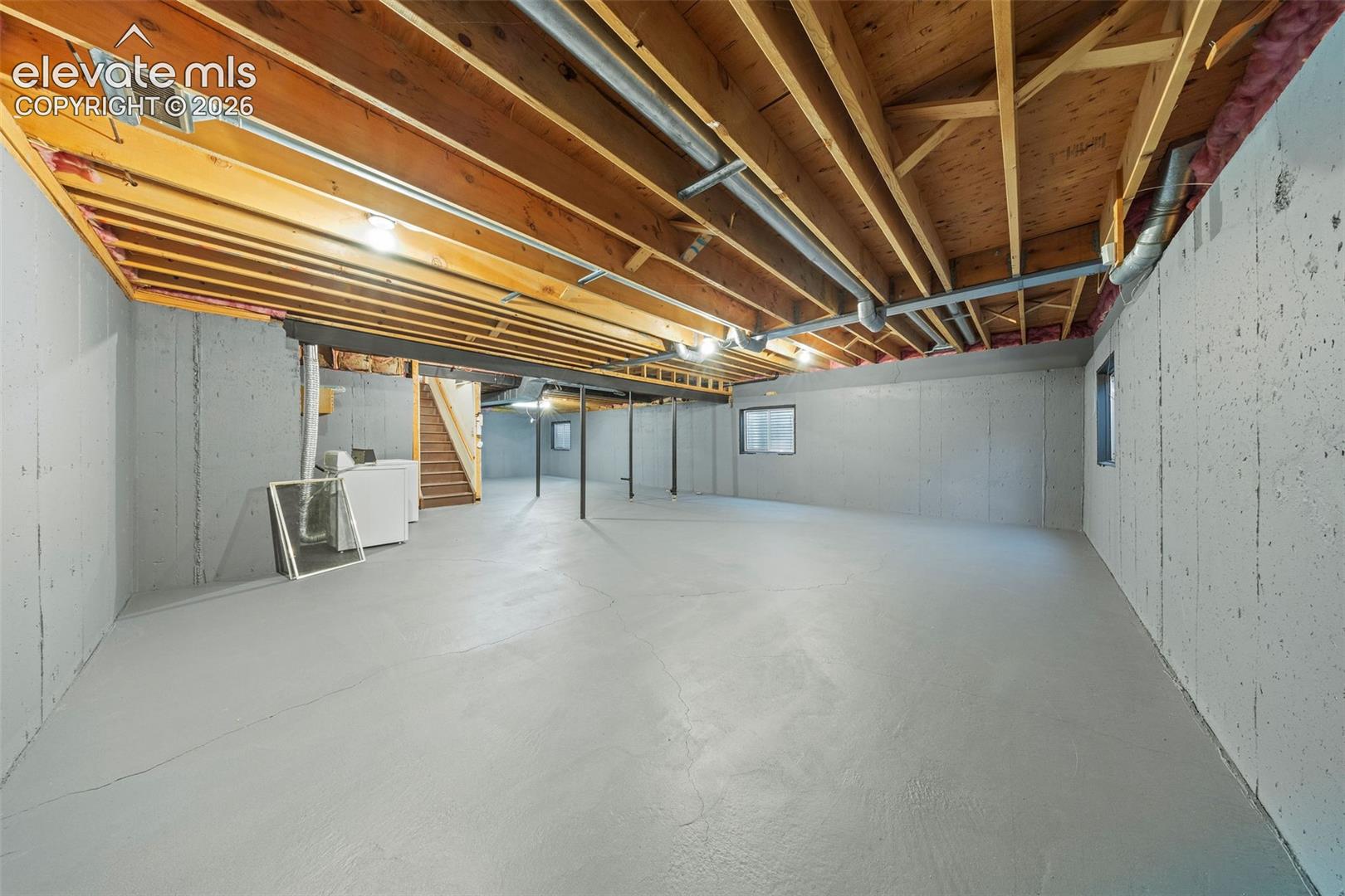 Unfinished lower level featuring exposed wood joist ceilings, poured concrete foundation walls, painted concrete flooring, and multiple windows