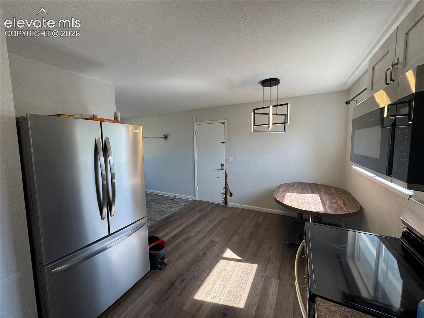 Stainless steel French door refrigerator, wood-finish flooring, modern pendant lighting fixture, built-in microwave, and electric range