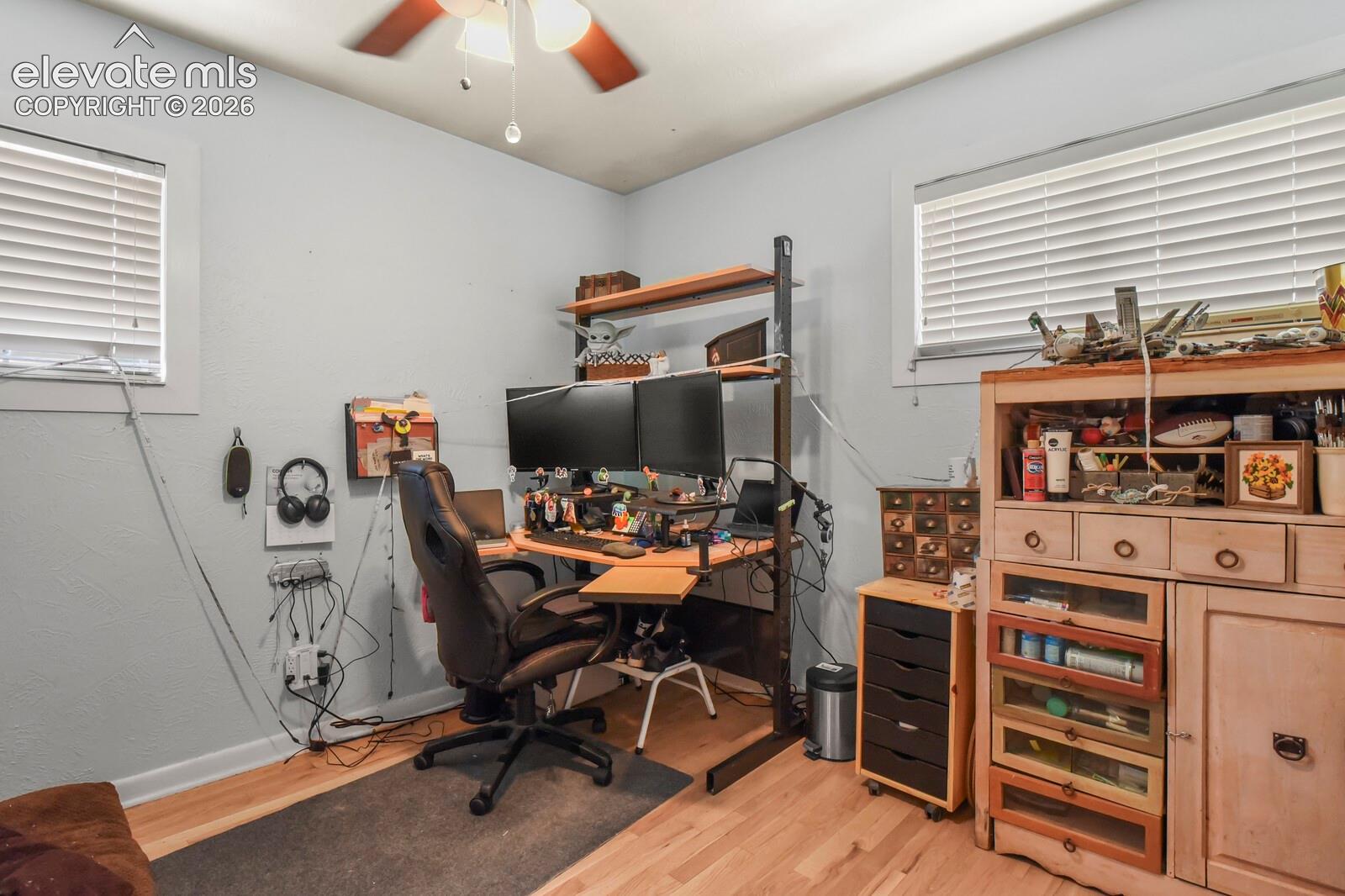 Wood-finish flooring, ceiling fan with integrated lighting, and multiple windows with blinds