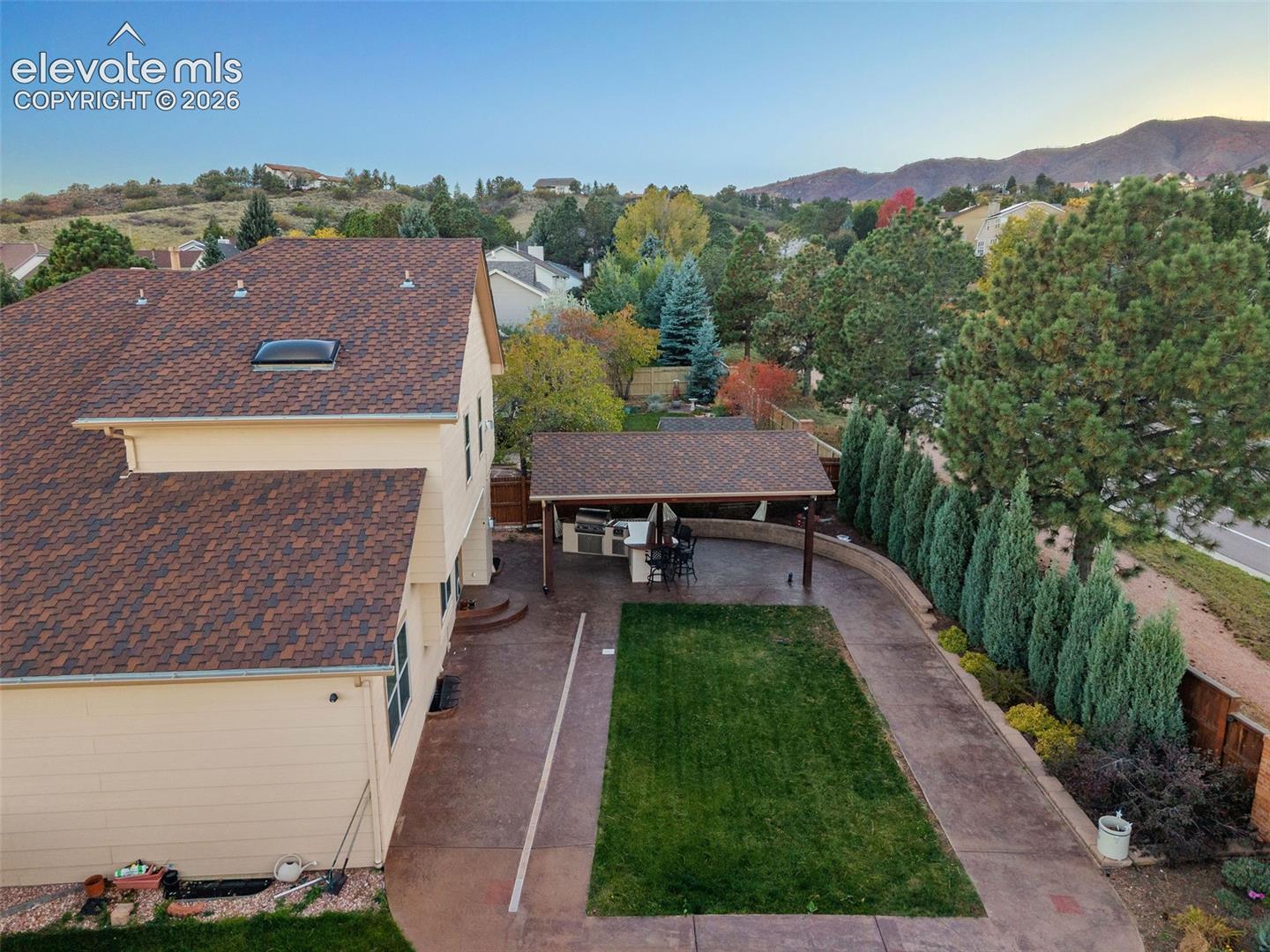 Backyard featuring a covered patio, built-in outdoor kitchen, concrete hardscaping, manicured lawn, and perimeter landscaping, with mountain scenery