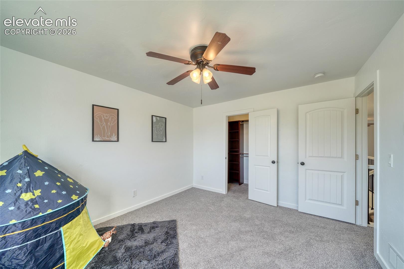 Carpeted flooring, white walls, ceiling fan with integrated lighting, two-panel interior doors, and a built-in closet with shelving