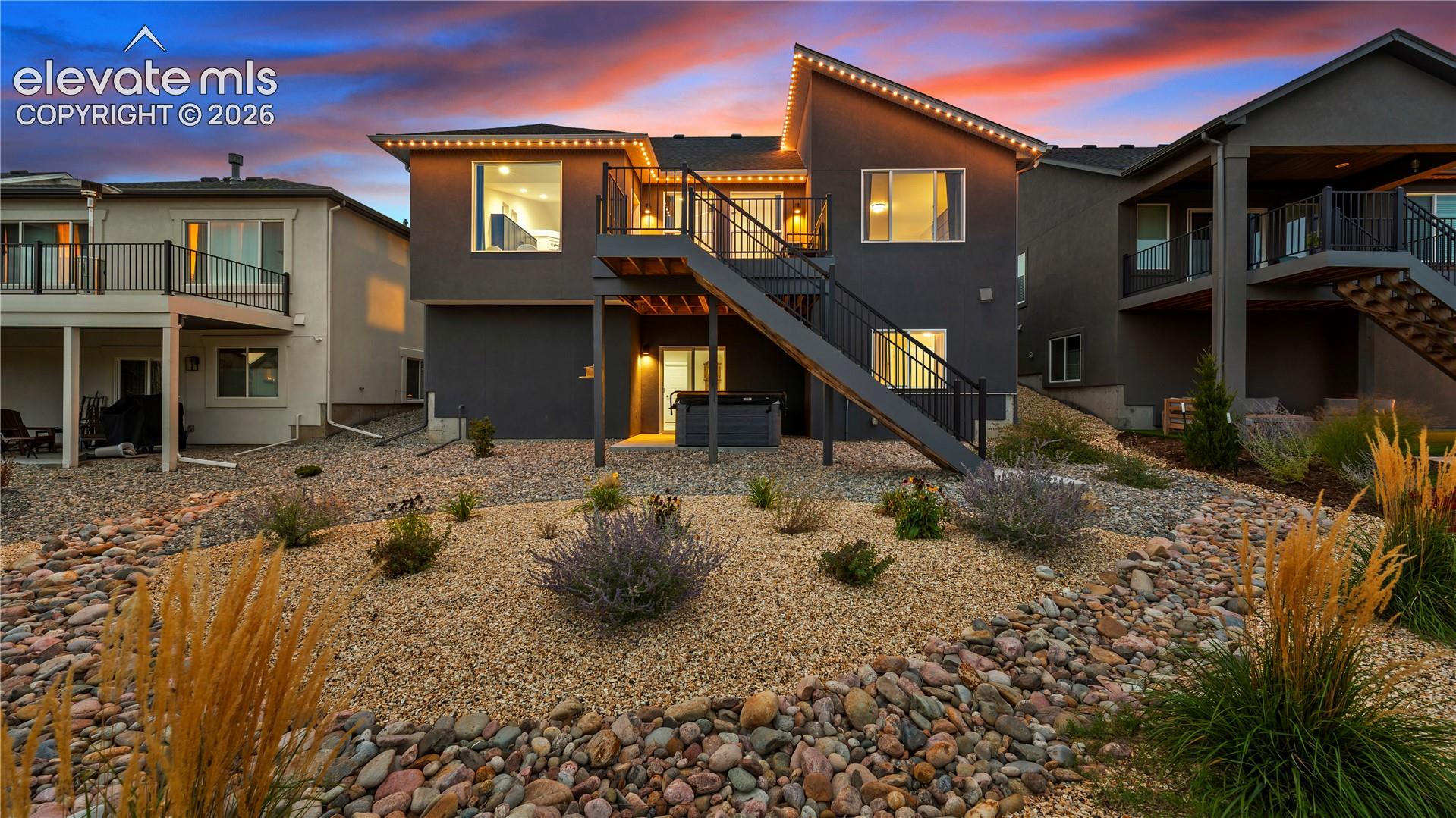 Contemporary residence featuring a multi-level deck, metal railing system, exterior staircase, low-maintenance gravel landscaping, and concrete patio