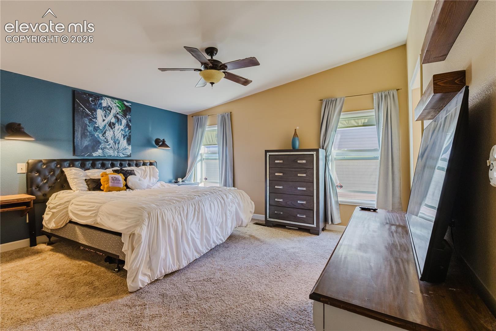 Vaulted ceiling with a ceiling fan, dual windows, and wall-mounted shelving