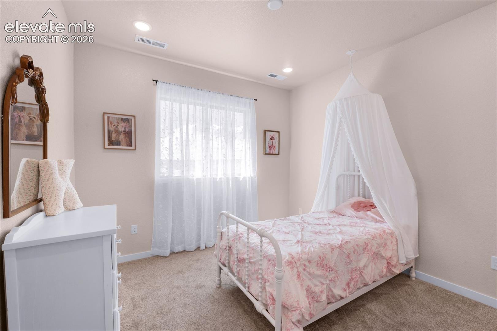 Recessed lighting, light-toned carpeting, and a window with sheer white curtains