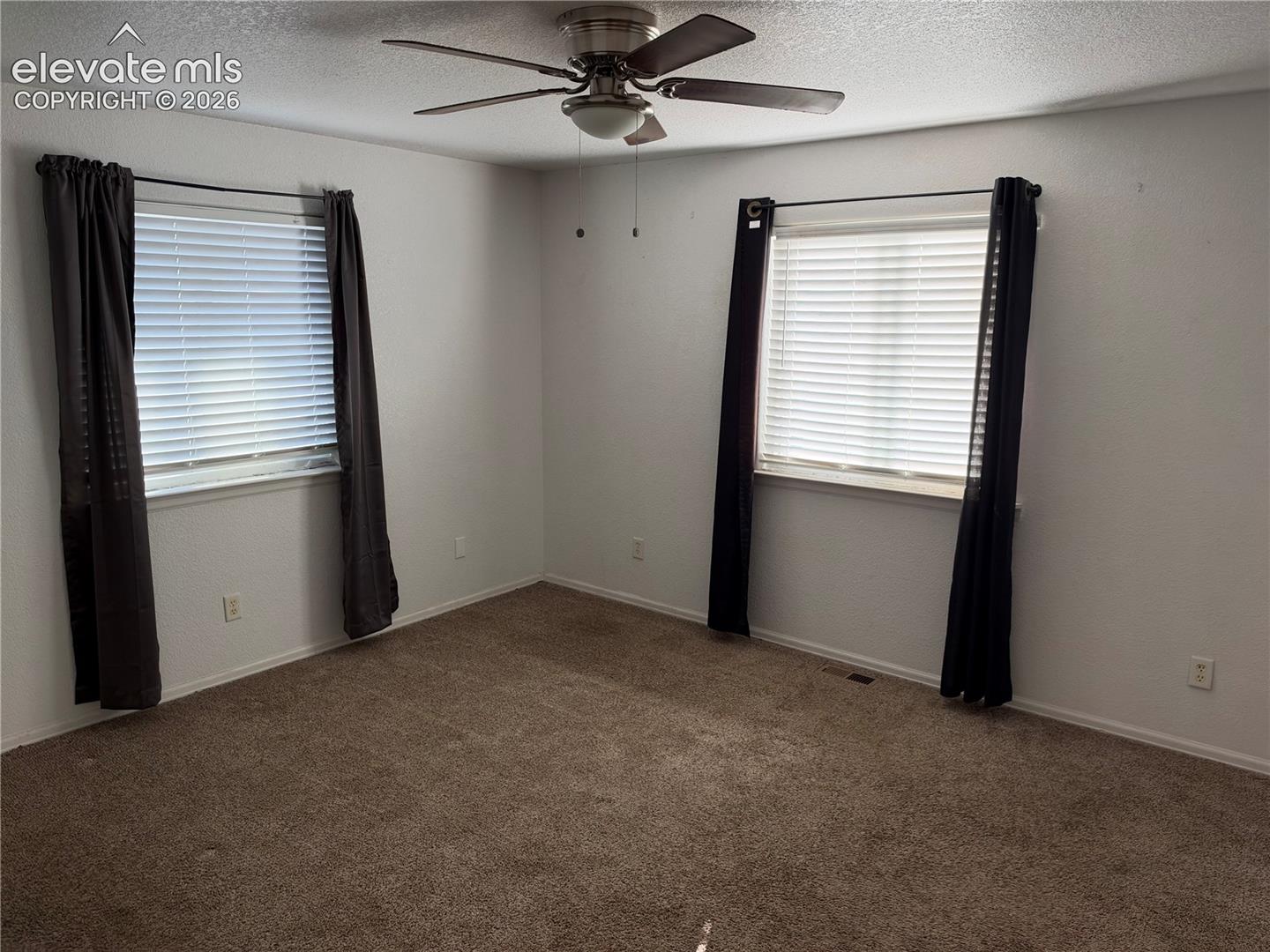 Neutral-toned room featuring neutral carpeting, two windows with horizontal blinds, and a ceiling-mounted fan with integrated lighting