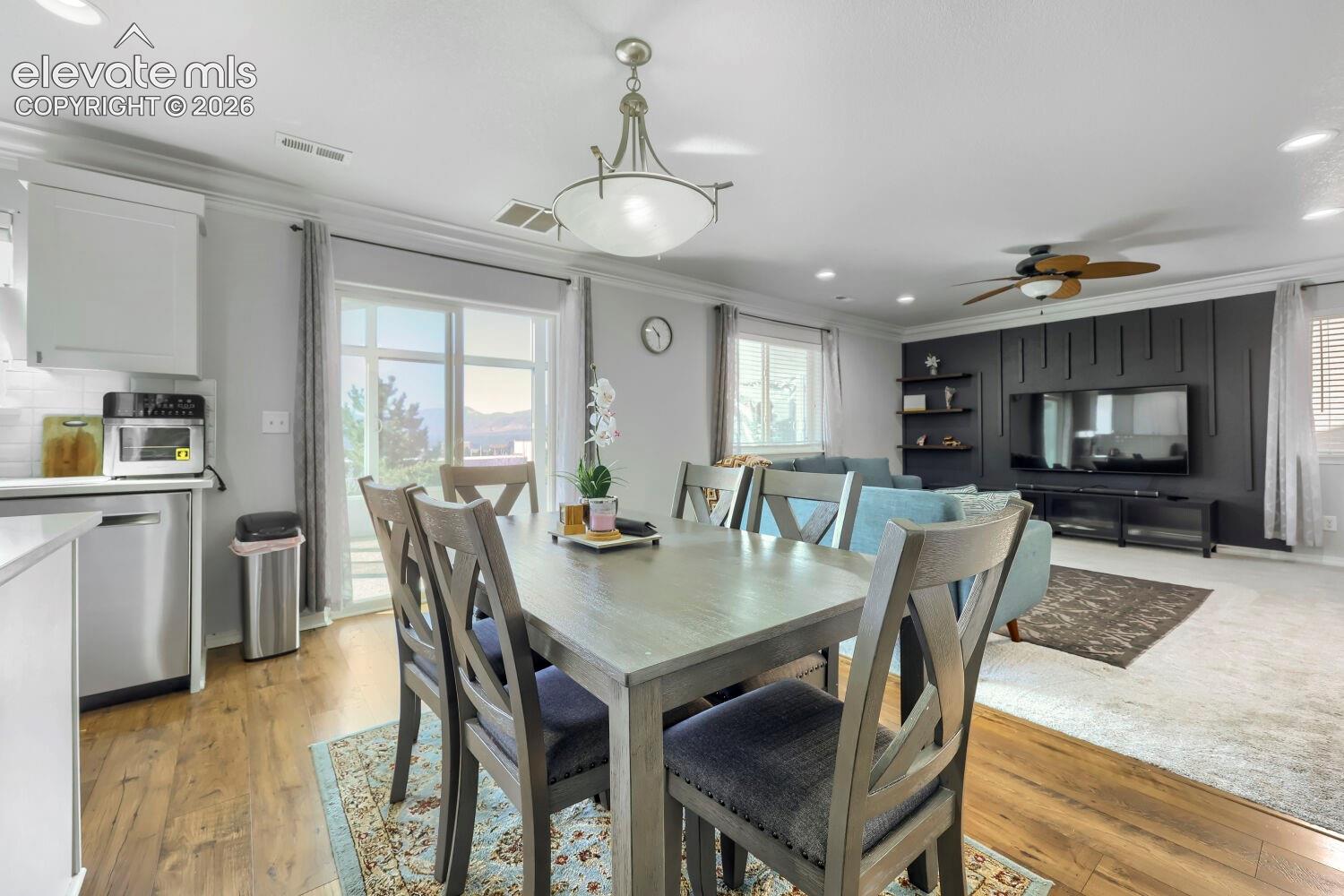 Open-concept living space featuring a custom charcoal-toned vertical slat accent wall, recessed lighting, wood-finish flooring, and a multi-light pendant fixture