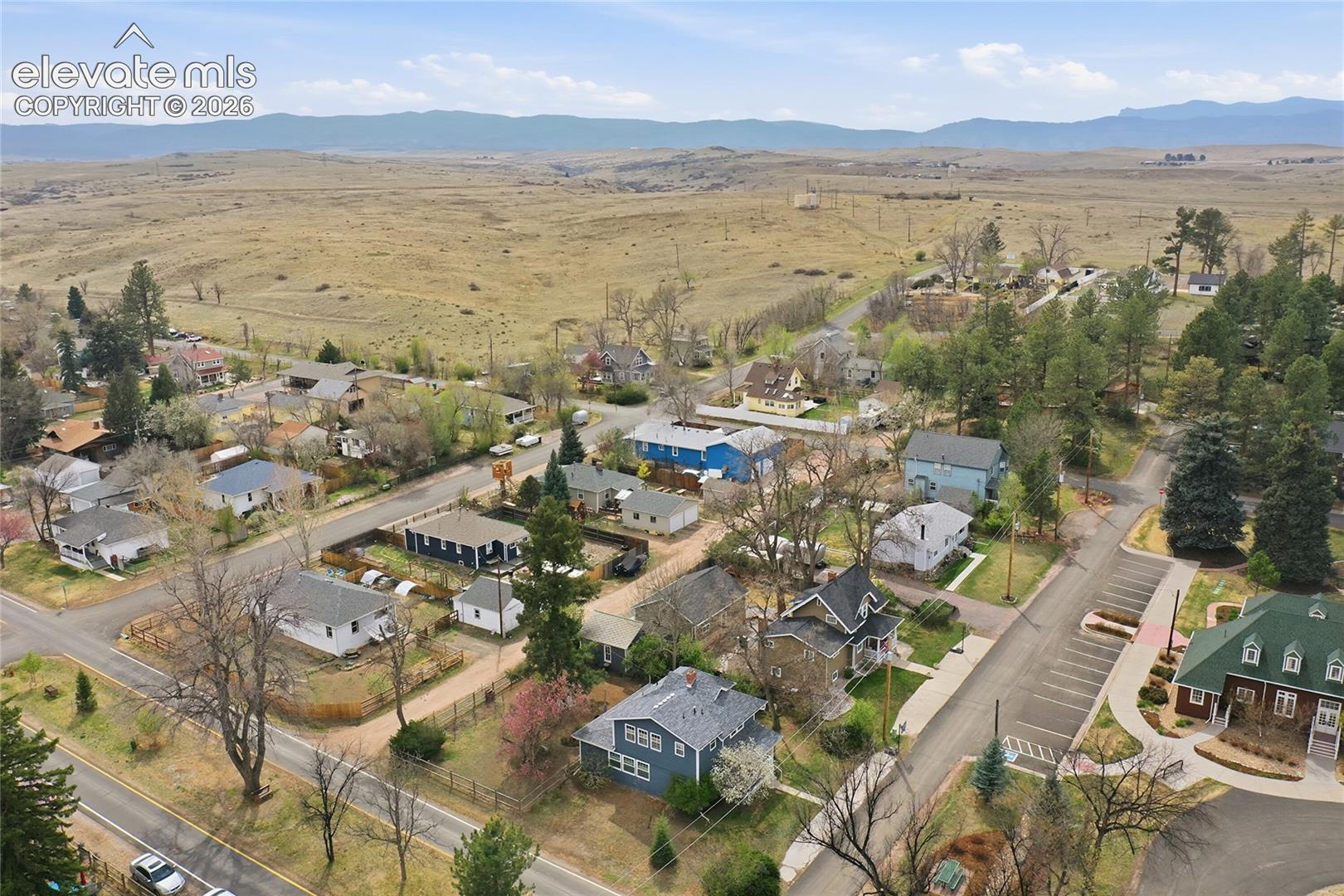 Aerial perspective of a residential neighborhood featuring paved streets, mature deciduous and coniferous trees, and expansive mountain terrain in the distance