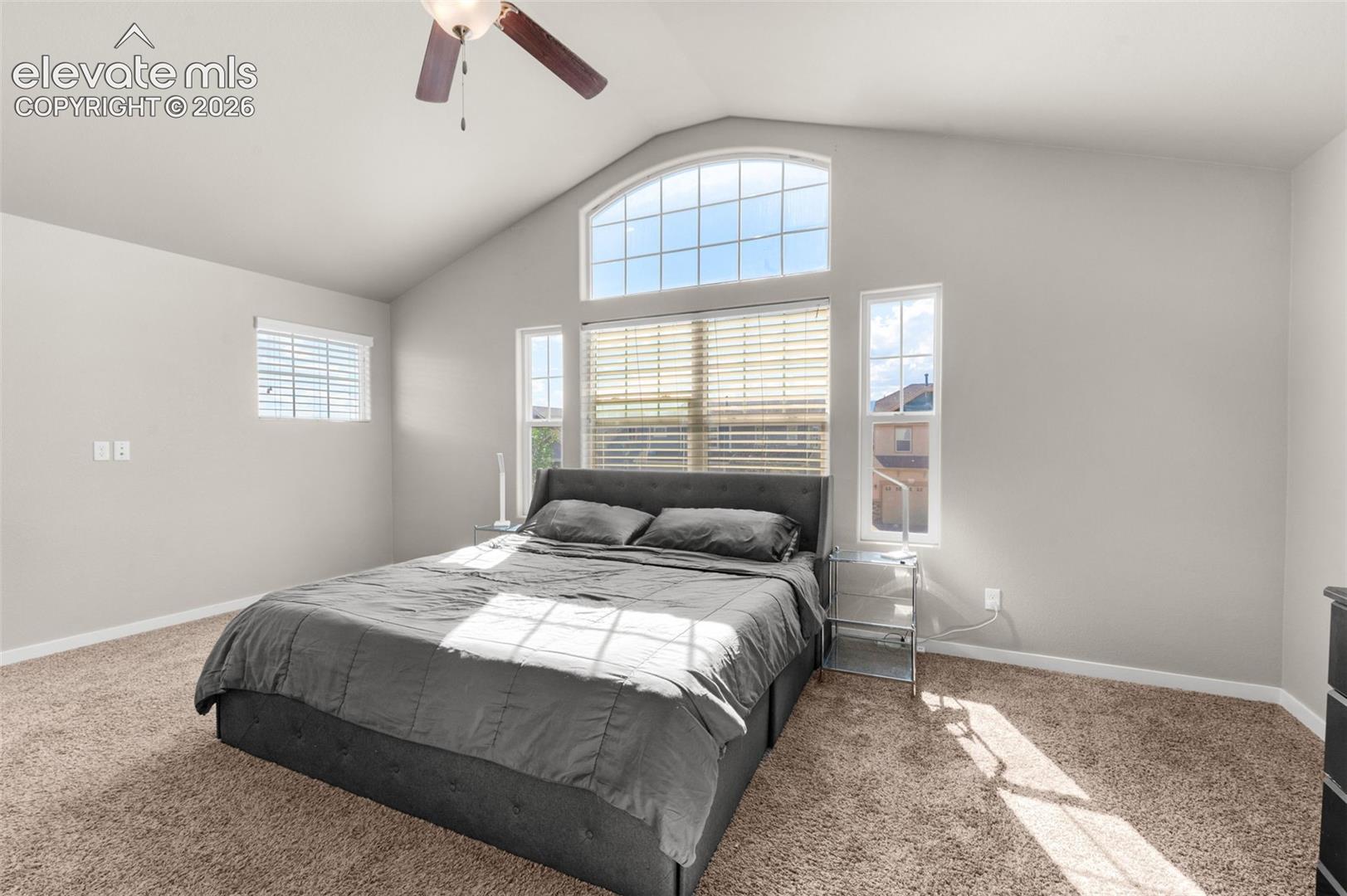Vaulted ceiling with a centrally mounted ceiling fan, arched window, and large windows with horizontal blinds