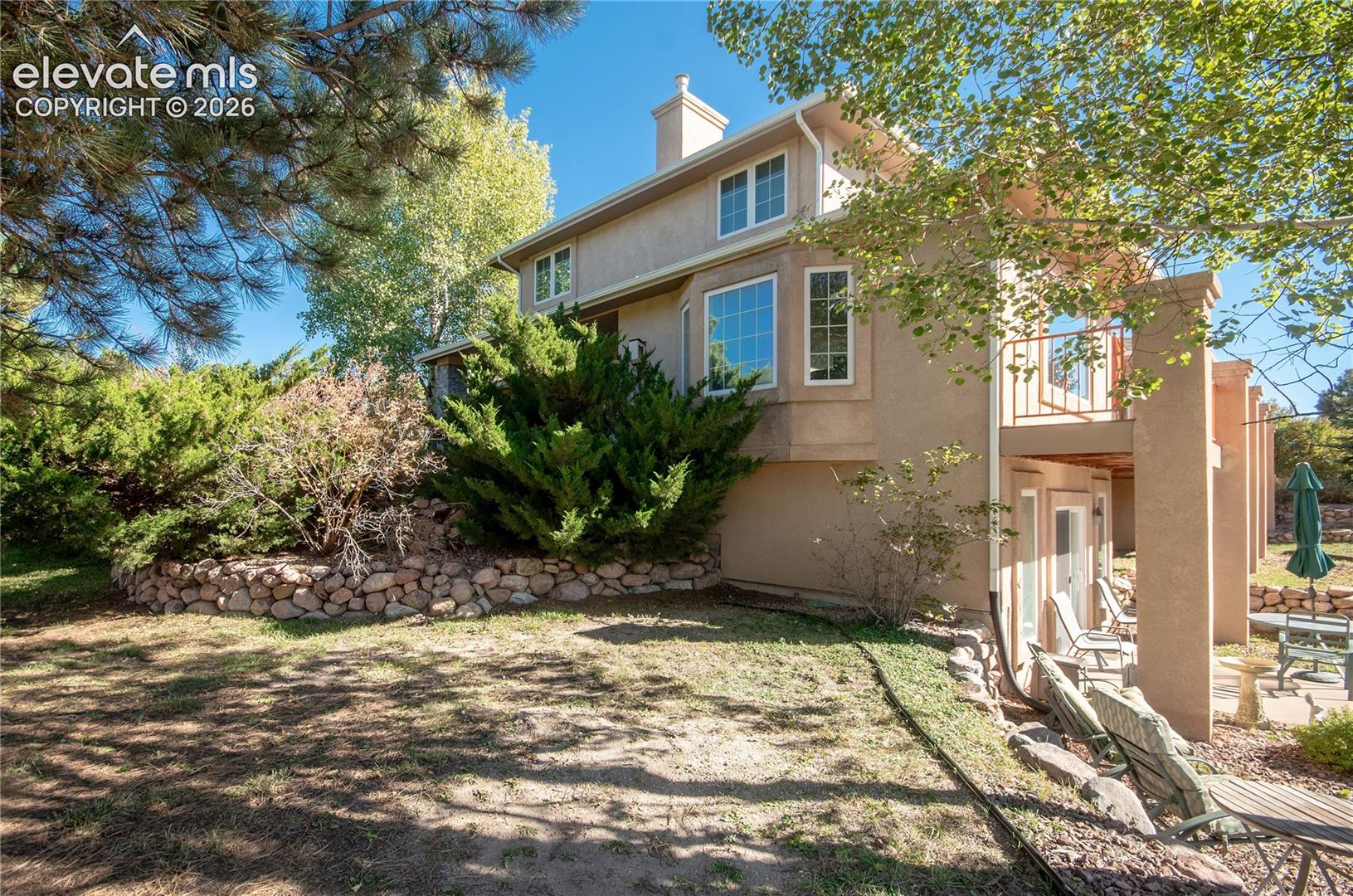 Stucco exterior featuring multiple windows, a second-story balcony with metal railing, and a stone retaining wall