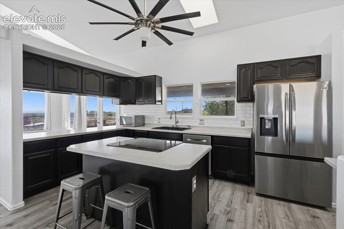 Kitchen featuring dark cabinetry, solid surface countertops, a white subway tile backsplash, stainless steel appliances, and wood-finish flooring