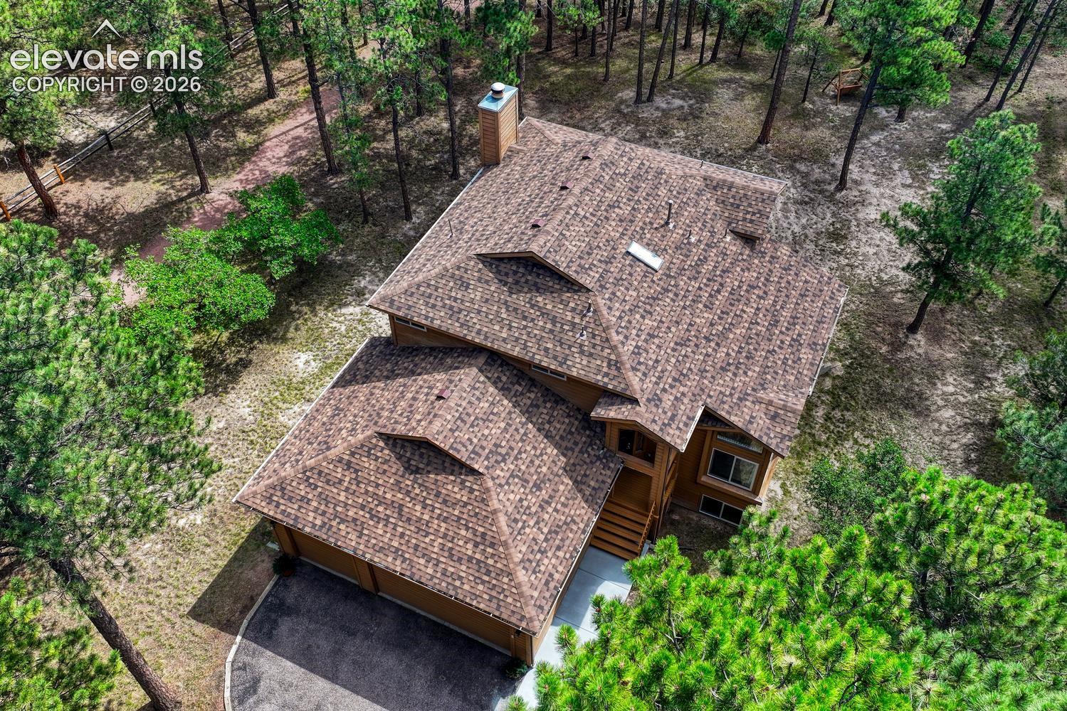 Multi-level residence featuring a textured shingle roof, chimney, multi-car garage, and wooded grounds